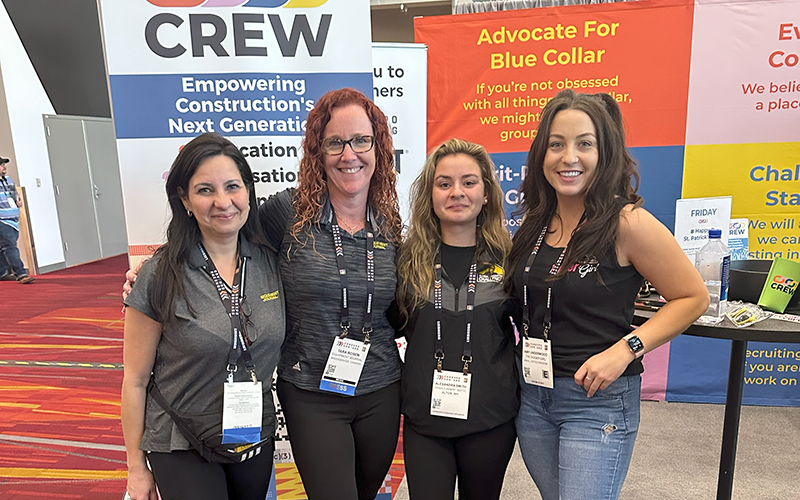 Amy posing with 4 people at CONEXPO-CON/AGG with banners in the background