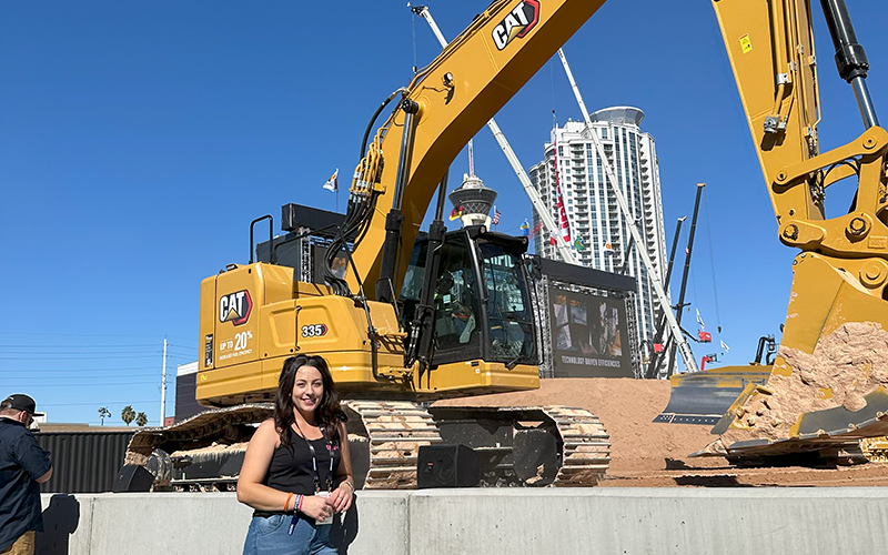 Amy Underwood posing in front of a CAT excavator at CONEXPO-CON/AGG