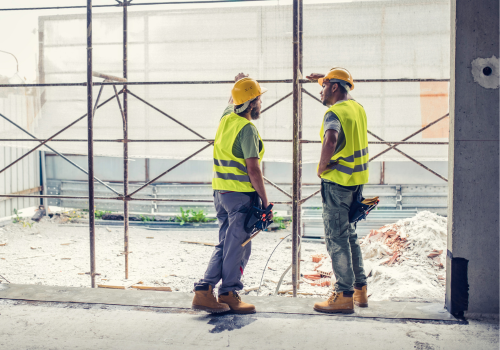 Construction workers wearing reflective clothing discussing at construction site.