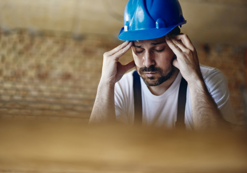 Exhausted construction worker holding his head in pain at construction site.