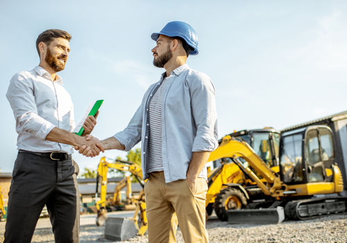 Builder choosing heavy machinery for construction with a sales consultant standing with some documents on the open ground of a shop with special vehicles