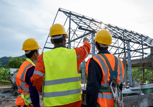 Engineer technician watching team of workers on high steel platform,Engineer technician Looking Up and Analyzing an Unfinished Construction Project.