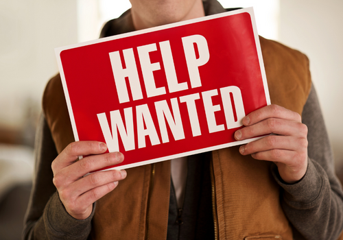 Trades worker holding a help wanted sign