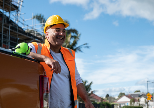 A happy construction work leaning against the back of a car