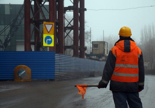 Male worker in uniform with flag standing across the road preventing traffic in the construction area