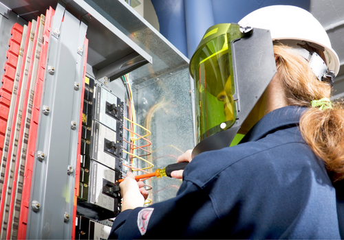  Electrician with arc flash protective clothing performing work in an energized panel with a happy smile